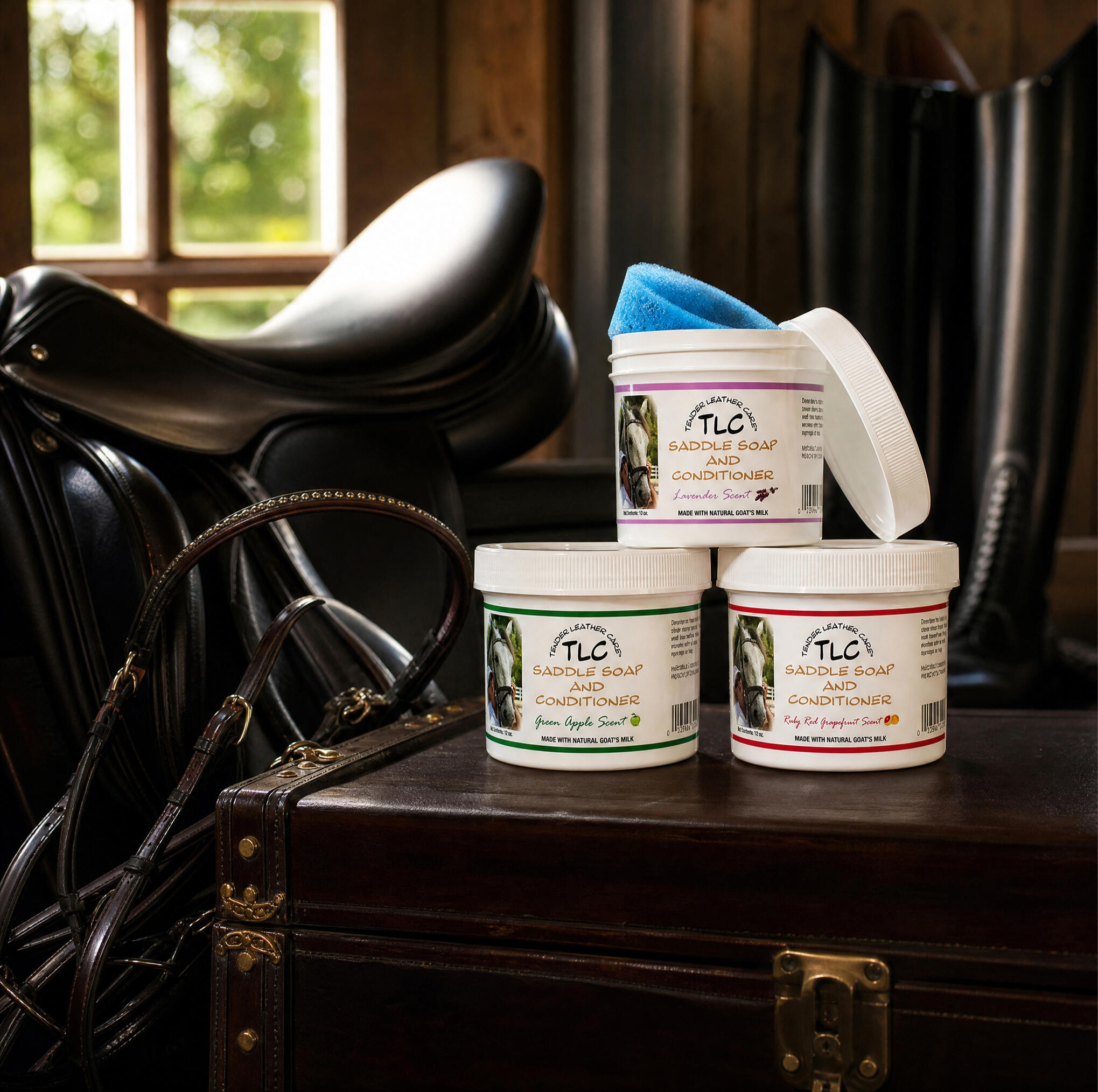 TLC Saddle Soap Product Family TLC Saddle Soap leather cleaner and conditioner product family displayed on a tack trunk in a horse barn. Available in Lavender, Green Apple, and Ruby Red Grapefruit scents.
